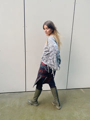 Person wearing a patterned sweater and jeans walking against a plain wall.