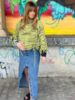 Woman wearing a green knitted sweater and denim skirt standing in front of a colorful graffiti wall.