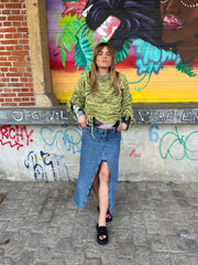 Person wearing a green sweater and denim skirt standing in front of a colorful mural.